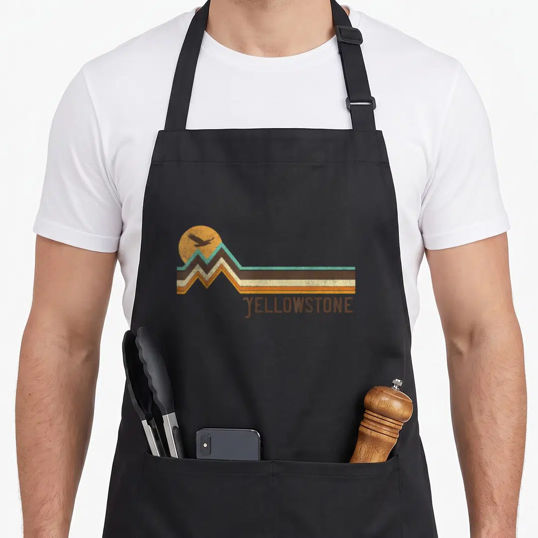 Distressed apron gift - Retro Yellowstone graphic with jagged peaks, stripes, bird silhouette, and brown text — shown on a black cotton canvas apron against a white background