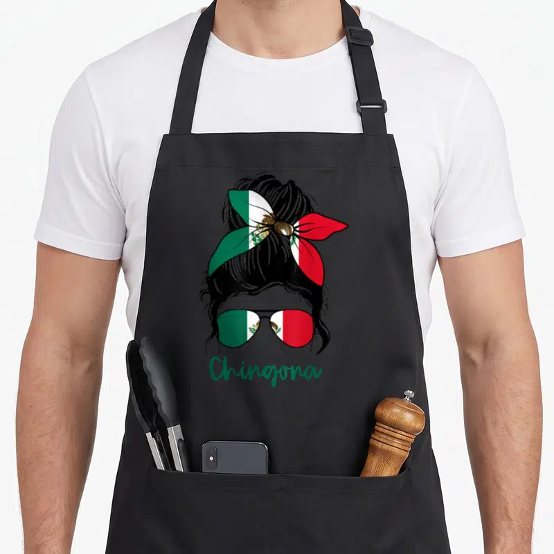 Chingona mexican apron - Cartoon woman head with bun and sunglasses filled with Mexican flag pattern and green text — shown on a black cotton canvas apron against a white background
