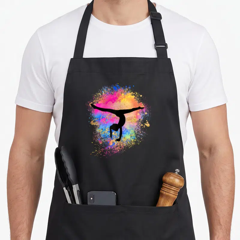 Gymnastic rainbow apron - Black gymnast handstand silhouette on pink blue yellow paint splatter — shown on a black cotton canvas apron against a white background