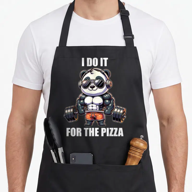 Panda bodybuilder apron - Muscular cartoon panda lifting barbell with text I DO IT FOR THE PIZZA — shown on a black cotton canvas apron against a white background
