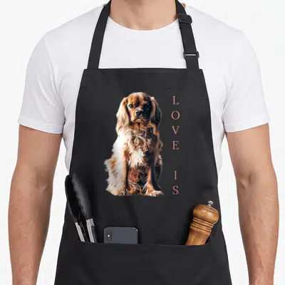 English cocker spaniel apron - Photo of brown and white dog with vertical pink LOVE IS text — shown on a black cotton canvas apron against a white background