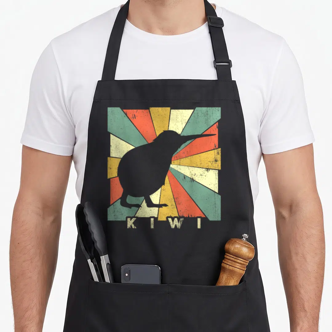 Kiwi birds apron - Grey kiwi bird silhouette on retro red yellow green sunburst with cream text — shown on a black cotton canvas apron against a white background