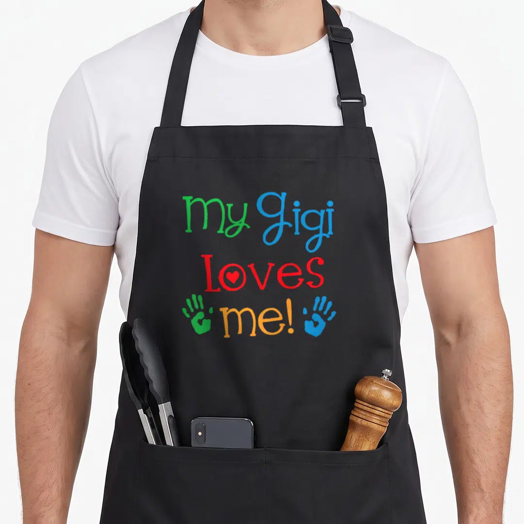 Gigi grandchild apron - Stacked text my Gigi Loves me! with red heart in O and green blue handprints — shown on a black cotton canvas apron against a white background