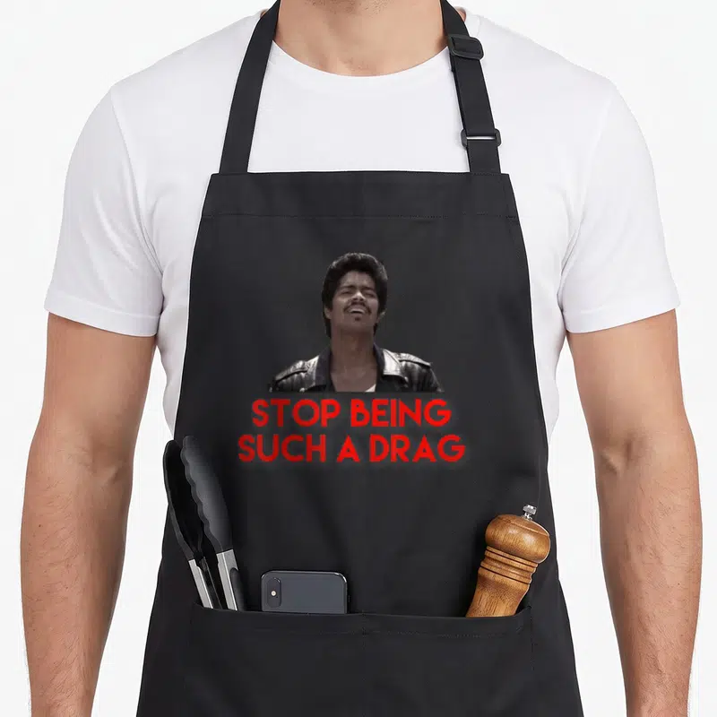 Stop drag apron - Man in leather jacket above red text reading STOP BEING, SUCH A DRAG — shown on a black cotton canvas apron against a white background