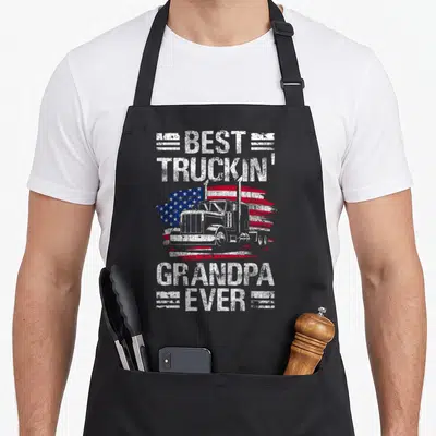 Grandpa semi truck apron - Best Truckin Grandpa Ever text over white semi truck and distressed red white blue flag — shown on a black cotton canvas apron against a white background