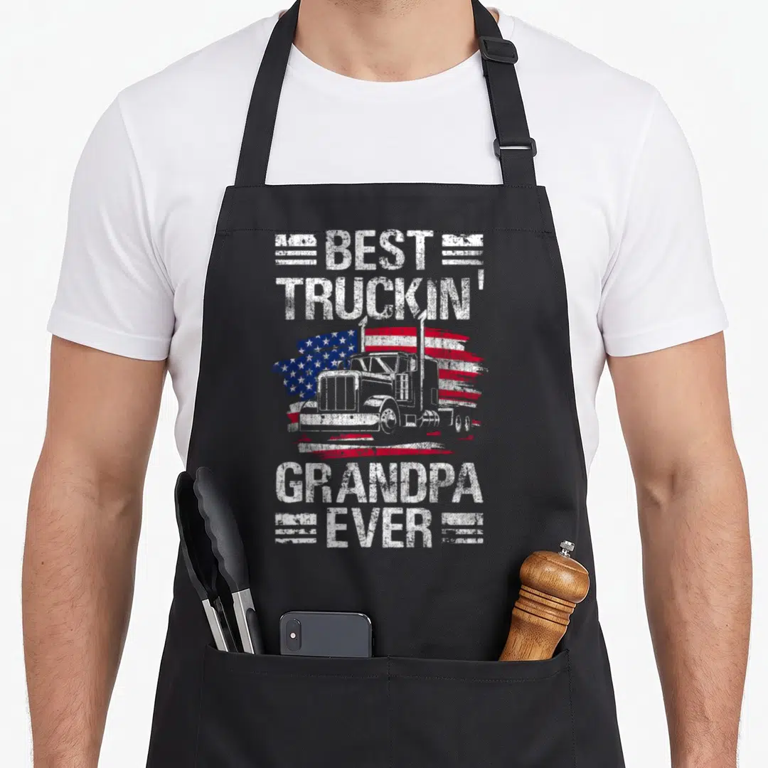 Grandpa semi truck apron - Best Truckin Grandpa Ever text over white semi truck and distressed red white blue flag — shown on a black cotton canvas apron against a white background