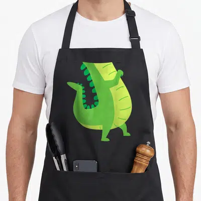 Costume animal apron - Stylized green alligator with open mouth and light green belly stripes — shown on a black cotton canvas apron against a white background