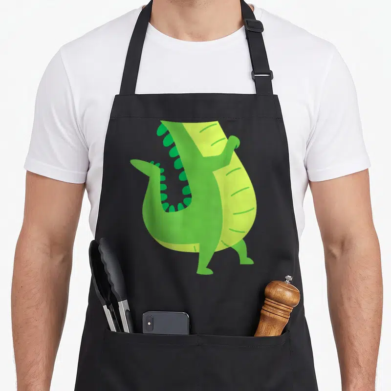 Costume animal apron - Stylized green alligator with open mouth and light green belly stripes — shown on a black cotton canvas apron against a white background