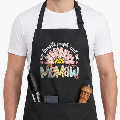 Girly mother's day aprons - Pink daisy and teal floral letters spelling memaw with bow accents — shown on a black cotton canvas apron against a white background