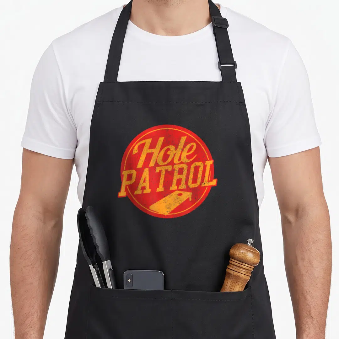 Hole game aprons - Distressed red circle with orange Hole PATROL text and bean bag shape below — shown on a black cotton canvas apron against a white background
