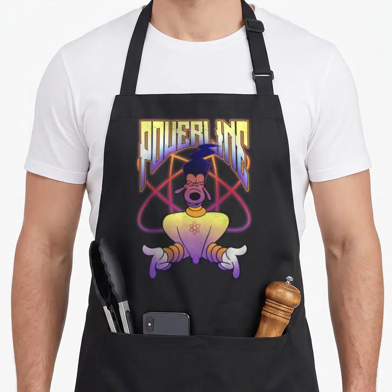 Movie x apron - POWERLINE text above cartoon dog character with atomic symbol on chest and large orbit background — shown on a black cotton canvas apron against a white background