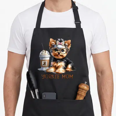 Latte dog apron - Cartoon Yorkshire Terrier with glasses and bow next to iced coffee cup and YORKIE MOM text — shown on a black cotton canvas apron against a white background