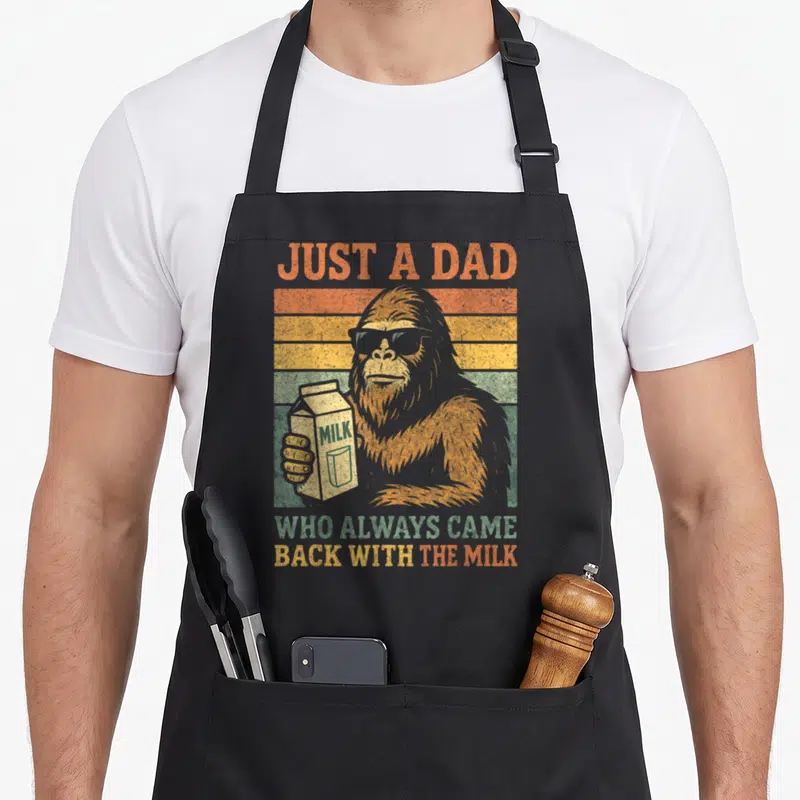 Bigfoot milk aprons - Retro sasquatch in sunglasses holding milk carton against orange and yellow stripes — shown on a black cotton canvas apron against a white background