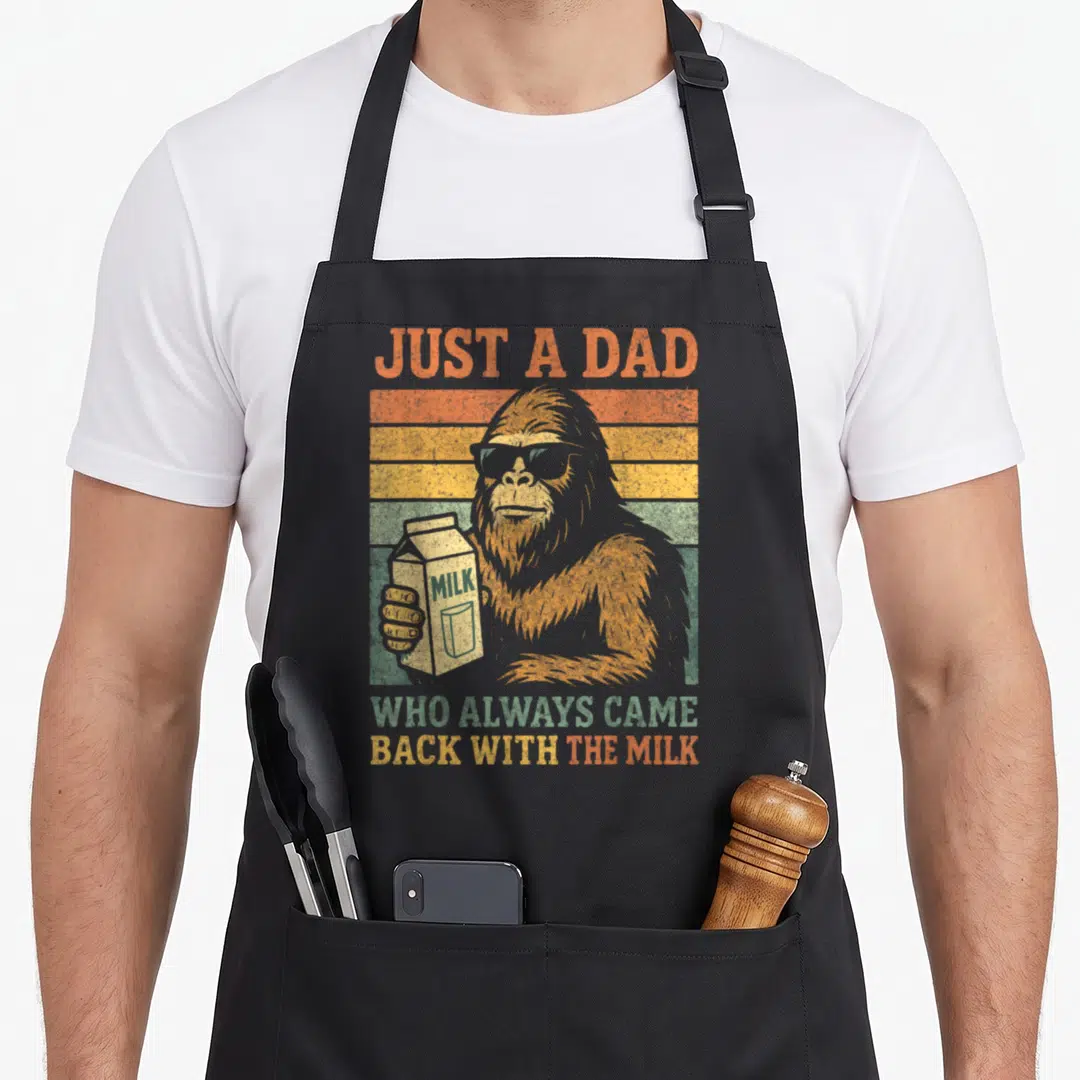 Bigfoot milk aprons - Retro sasquatch in sunglasses holding milk carton against orange and yellow stripes — shown on a black cotton canvas apron against a white background