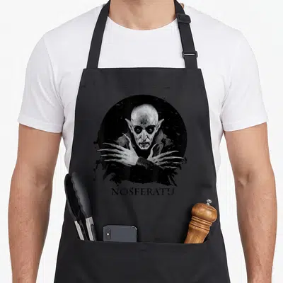 Cute vampire halloween apron - Nosferatu portrait in black circle with ink splatters and text below — shown on a black cotton canvas apron against a white background