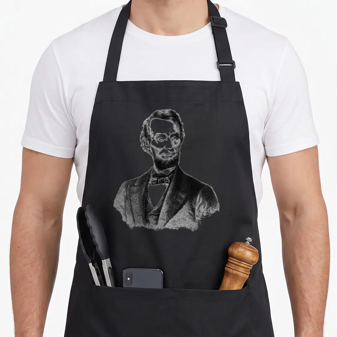 Abe crew apron - Realistic bust portrait of Abraham Lincoln in black and grey tones — shown on a black cotton canvas apron against a white background