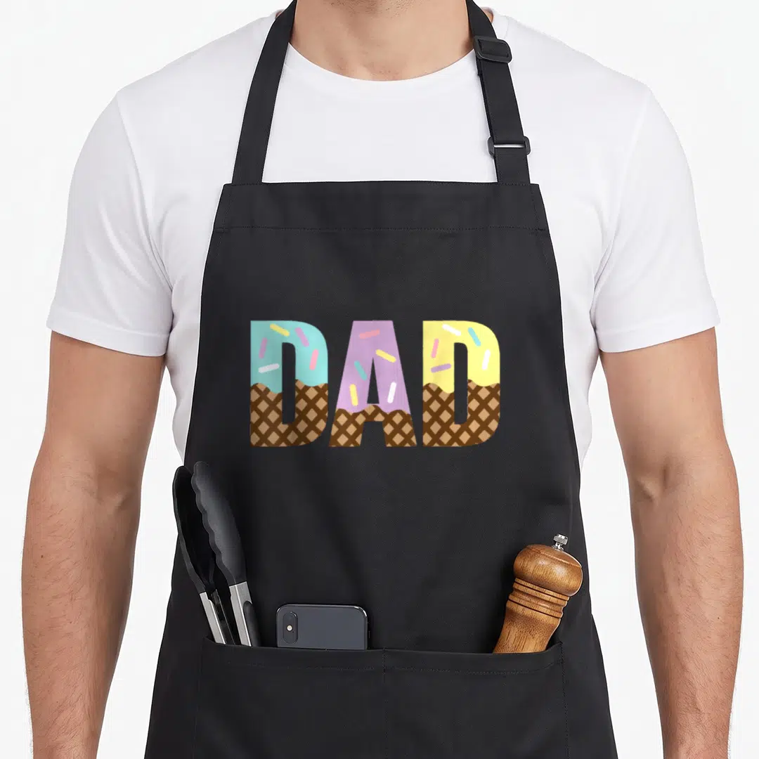 Sweet father day apron - DAD text shaped like waffle cones with blue purple and yellow frosting and sprinkles — shown on a black cotton canvas apron against a white background