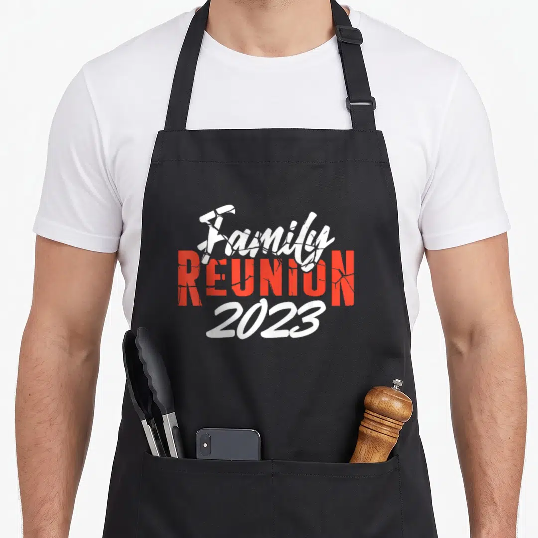 Family reunion gathering apron - Stacked white script and cracked red block text reading Family REUNION 2023 — shown on a black cotton canvas apron against a white background