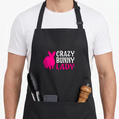 Hare animal bunny apron - Pink rabbit silhouette beside stacked white and pink Crazy Bunny Lady text — shown on a black cotton canvas apron against a white background