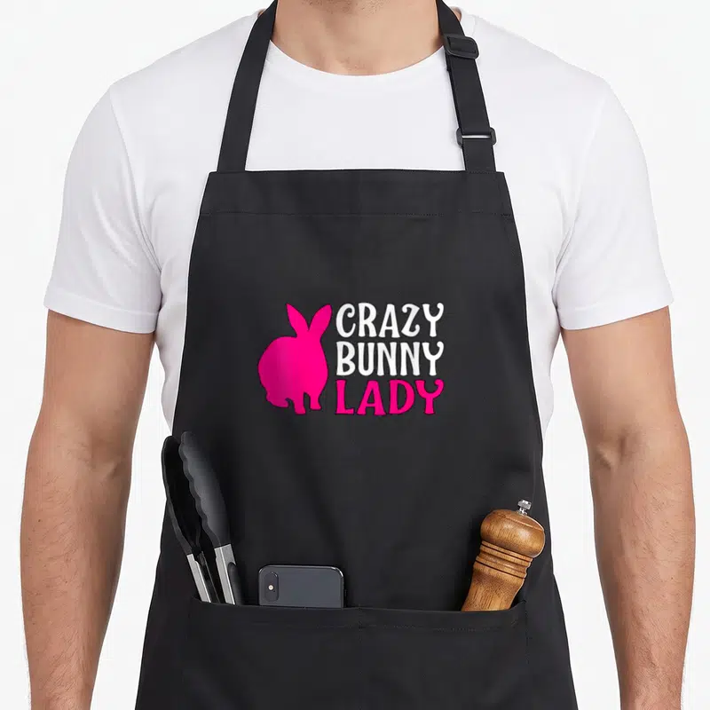 Hare animal bunny apron - Pink rabbit silhouette beside stacked white and pink Crazy Bunny Lady text — shown on a black cotton canvas apron against a white background