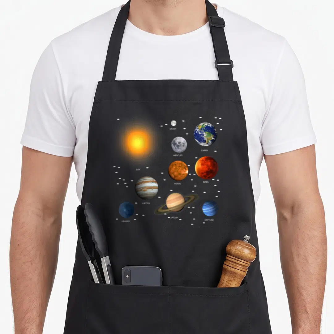 Our science apron - Solar system photo print with labeled planets sun earth jupiter saturn in blue yellow red grey — shown on a black cotton canvas apron against a white background