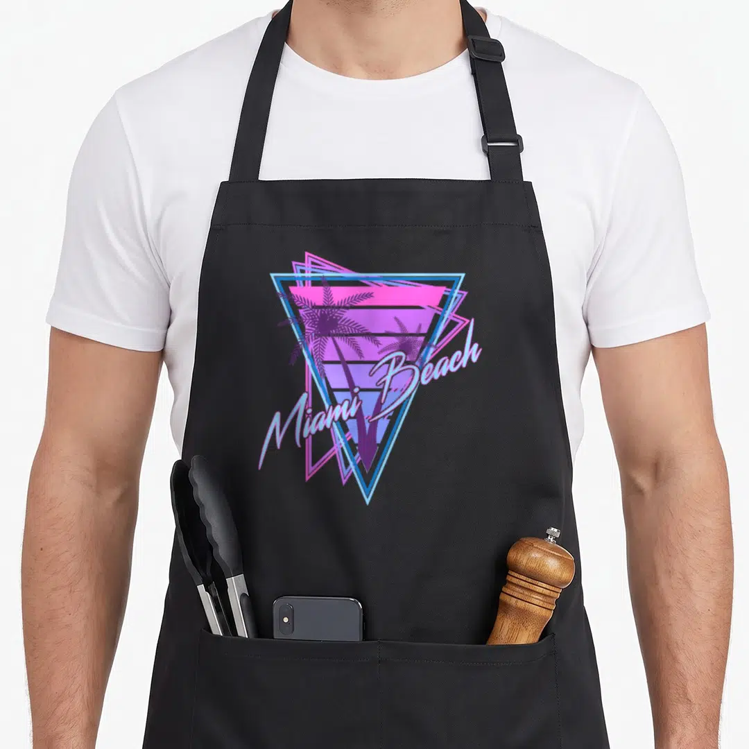 Miami 80s apron - Two palm trees inside nested triangle with striped sun and Miami Beach text in purple pink blue — shown on a black cotton canvas apron against a white background
