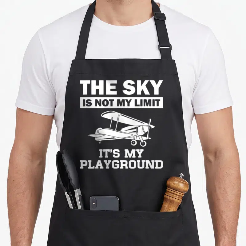 Airplane aircraft apron - White airplane centered between text reading The Sky Is Not My Limit It's My Playground — shown on a black cotton canvas apron against a white background