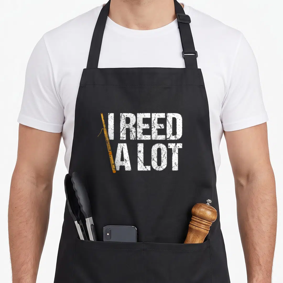 Symphony lot of aprons - Distressed white text I Reed A Lot with vertical orange oboe replacing the letter I — shown on a black cotton canvas apron against a white background