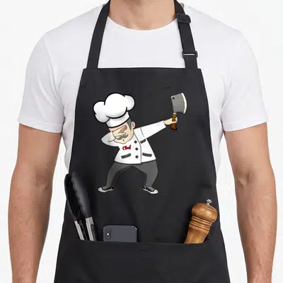 Dabbing culinary aprons - Cartoon chef dabbing holding cleaver white jacket red text grey pants — shown on a black cotton canvas apron against a white background
