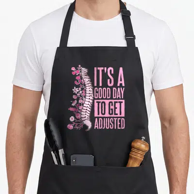 Assistant chiropractor apron - White spine entwined with pink flowers next to stacked pink text IT'S A GOOD DAY TO GET — shown on a black cotton canvas apron against a white background