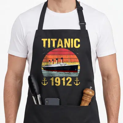 Titanic ocean apron - Retro ship illustration with TITANIC text, 1912 date, and two yellow anchors against a striped — shown on a black cotton canvas apron against a white background