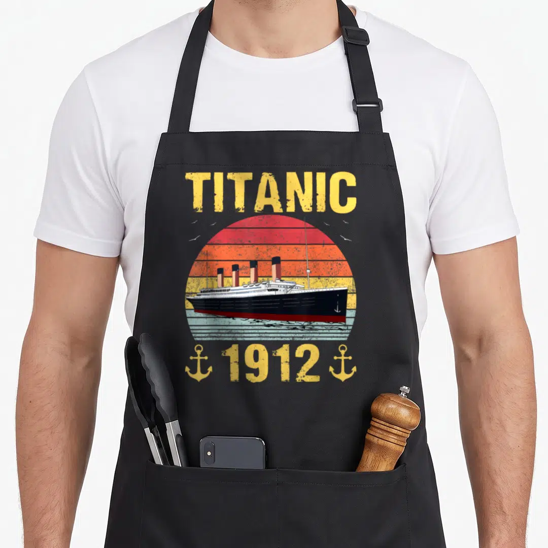 Titanic ocean apron - Retro ship illustration with TITANIC text, 1912 date, and two yellow anchors against a striped — shown on a black cotton canvas apron against a white background