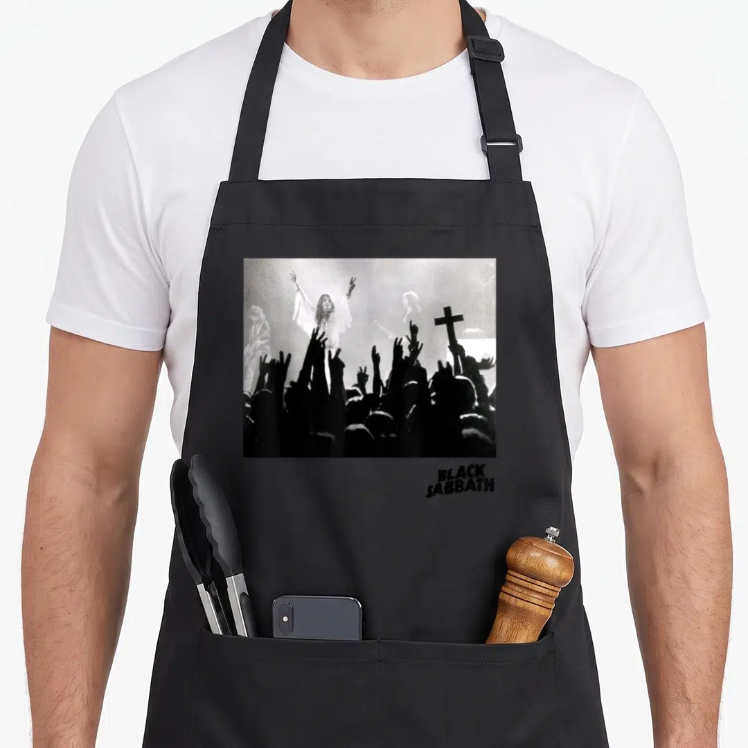 Hand black sabbath apron - Grayscale band photo with raised hands and cross, black text below — shown on a black cotton canvas apron against a white background