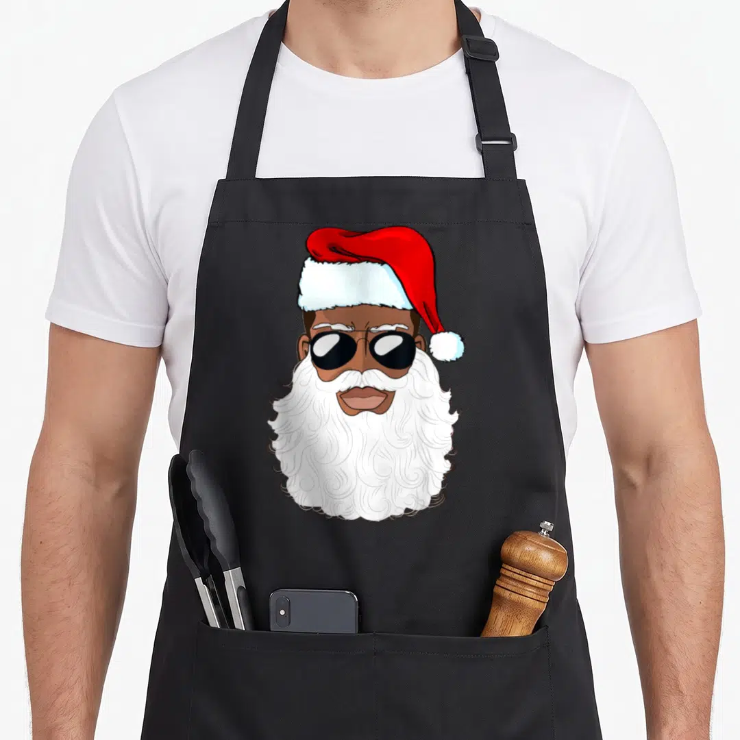 Xmas santa claus apron - Cartoon black Santa face with sunglasses, white beard, and red hat — shown on a black cotton canvas apron against a white background