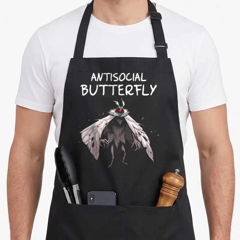 Cryptid butterfly apron - Cartoon moth with red eyes below stacked Antisocial Butterfly text on grey background — shown on a black cotton canvas apron against a white background