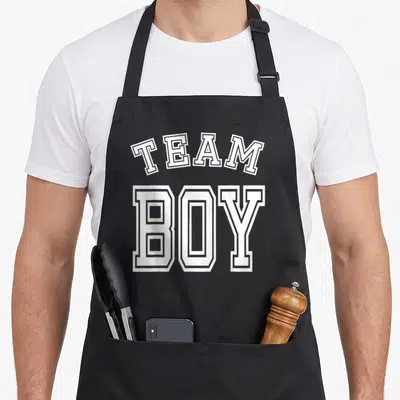 Baby funny babe apron - White arched TEAM BOY typography stacked on dark background — shown on a black cotton canvas apron against a white background