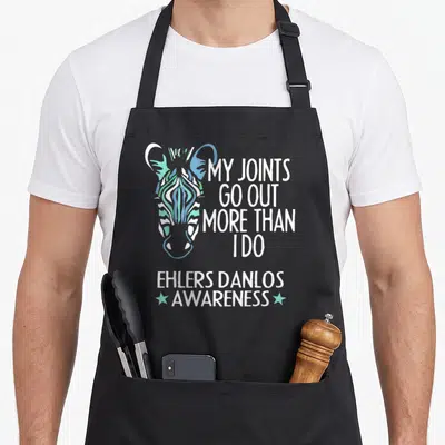 Ehler i love my zebra apron - Colorful zebra head with My Joints Go Out More Than I Do text and Ehlers Danlos Awareness — shown on a black cotton canvas apron against a white background