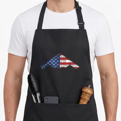 Bomber aircraft apron - B-2 stealth bomber silhouette filled with American flag stars and stripes schematic pattern — shown on a black cotton canvas apron against a white background