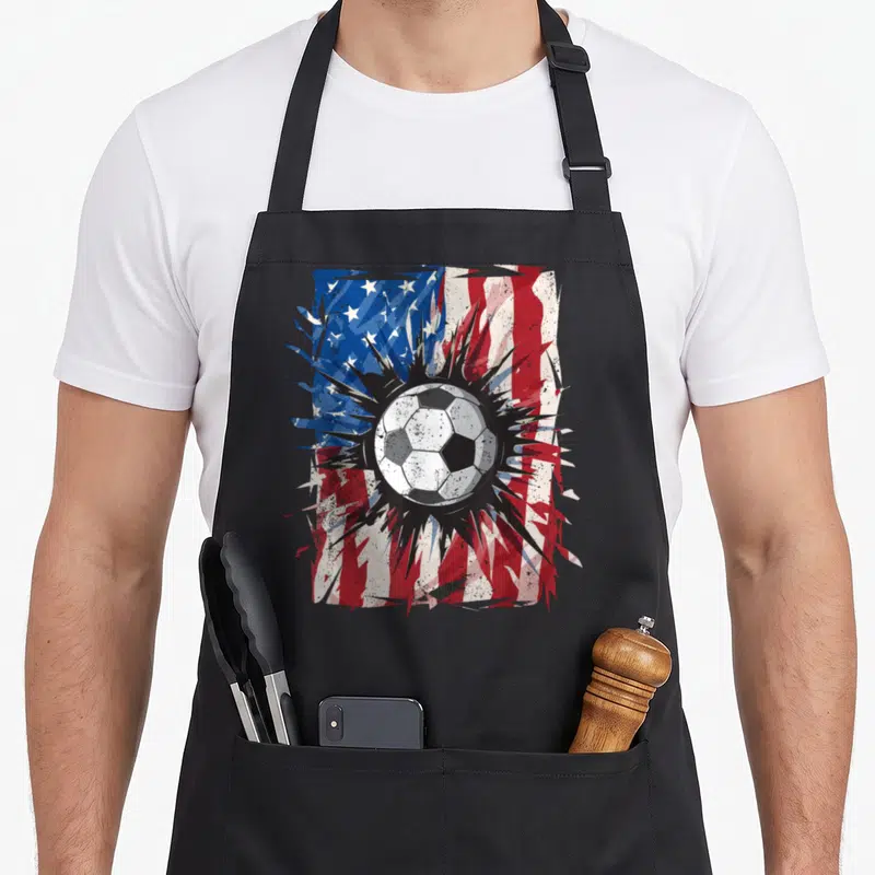 Soccer 4th of july apron - Distressed USA flag with soccer ball and black jagged explosion effect on black fabric — shown on a black cotton canvas apron against a white background