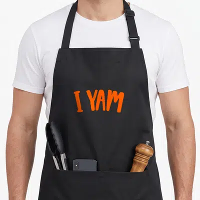 Yam sweet thanksgiving potato apron - Orange I YAM text on black bib apron — shown on a black cotton canvas apron against a white background