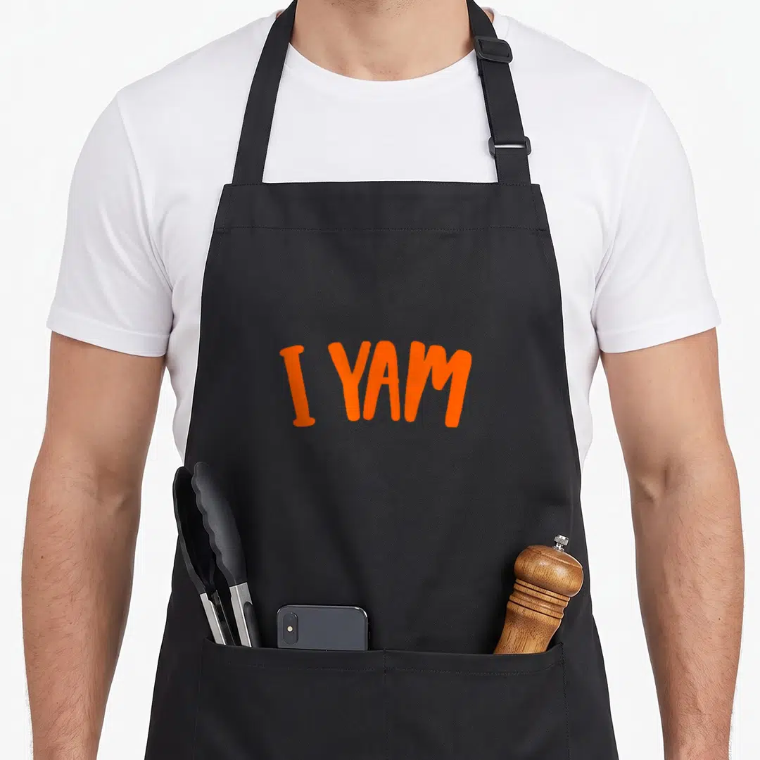 Yam sweet thanksgiving potato apron - Orange I YAM text on black bib apron — shown on a black cotton canvas apron against a white background