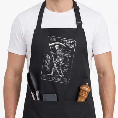 Gasp halloween apron - White line-art skeleton holding scythe inside rounded frame with text XIII and DEATH — shown on a black cotton canvas apron against a white background
