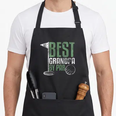 Grandpa grandad aprons - Distressed green and white text best grandpa by par with golf flag hole and ball graphic — shown on a black cotton canvas apron against a white background