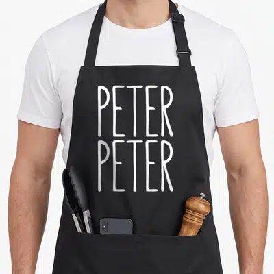 Peter eater pumpkin apron - White stacked text PETER PETER on grey background — shown on a black cotton canvas apron against a white background