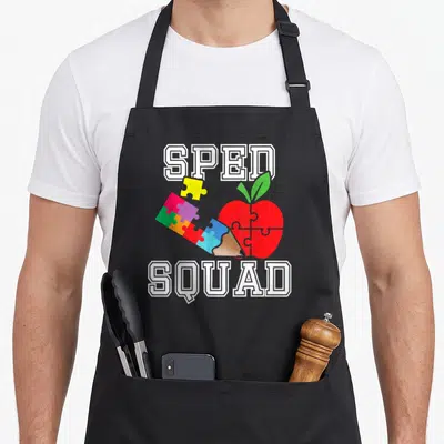 Sped education apron - Red apple puzzle pieces pencil SPED SQUAD text cartoon style — shown on a black cotton canvas apron against a white background