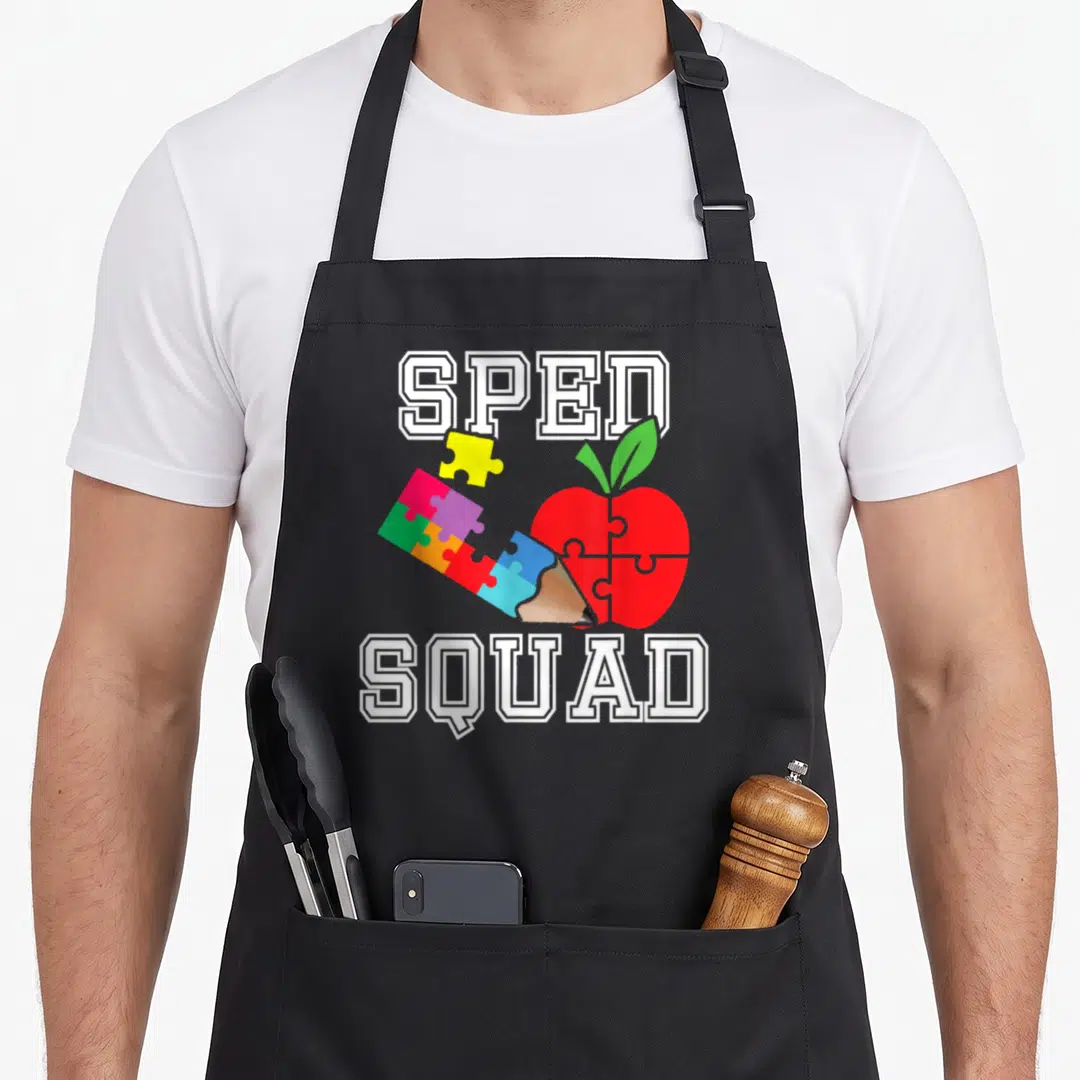 Sped education apron - Red apple puzzle pieces pencil SPED SQUAD text cartoon style — shown on a black cotton canvas apron against a white background