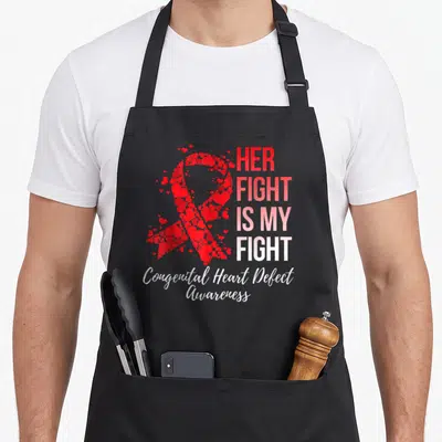 Fight congenital heart defect apron - Ribbon made of red hearts with stacked text Her Fight Is My Fight Congenital — shown on a black cotton canvas apron against a white background