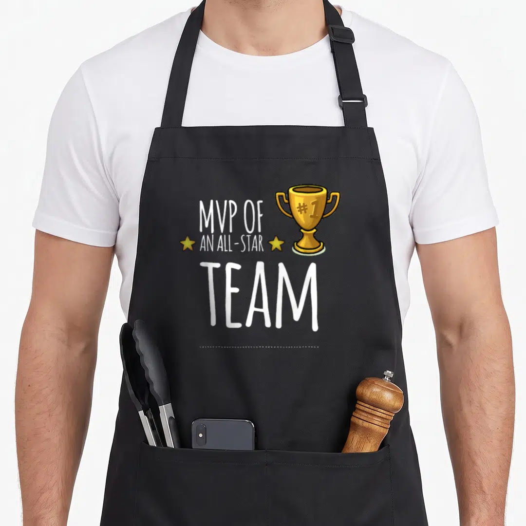 Mvp trophy apron - White MVP OF AN ALL-STAR TEAM text with gold trophy and two stars on black bib — shown on a black cotton canvas apron against a white background