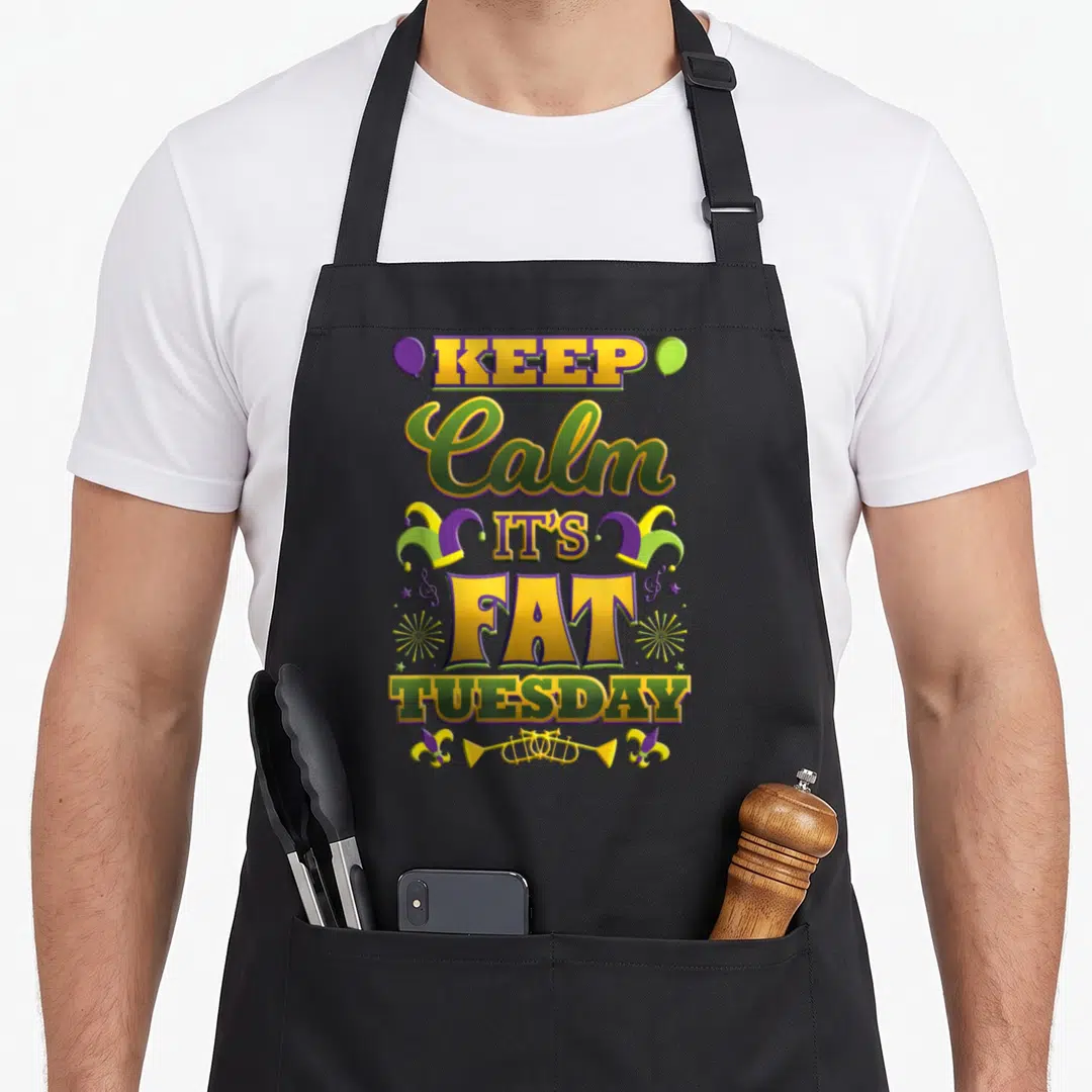 Mardi gras fat chef apron - Stacked KEEP Calm IT'S FAT TUESDAY text in purple green yellow with jester hats and trumpet — shown on a black cotton canvas apron against a white background