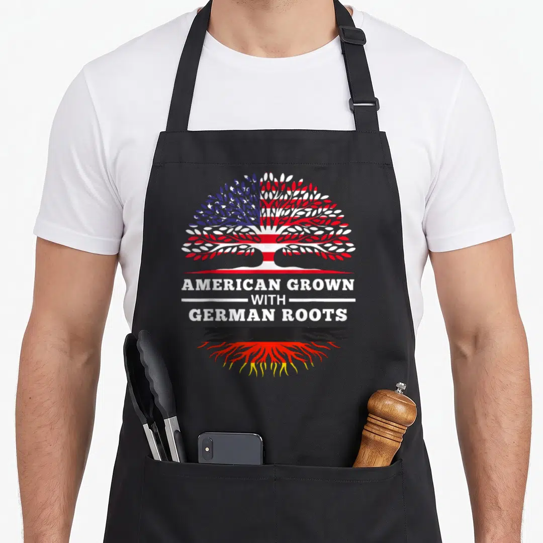 Root german apron - Tree with US flag leaves and German flag roots above AMERICAN GROWN WITH GERMAN ROOTS text — shown on a black cotton canvas apron against a white background
